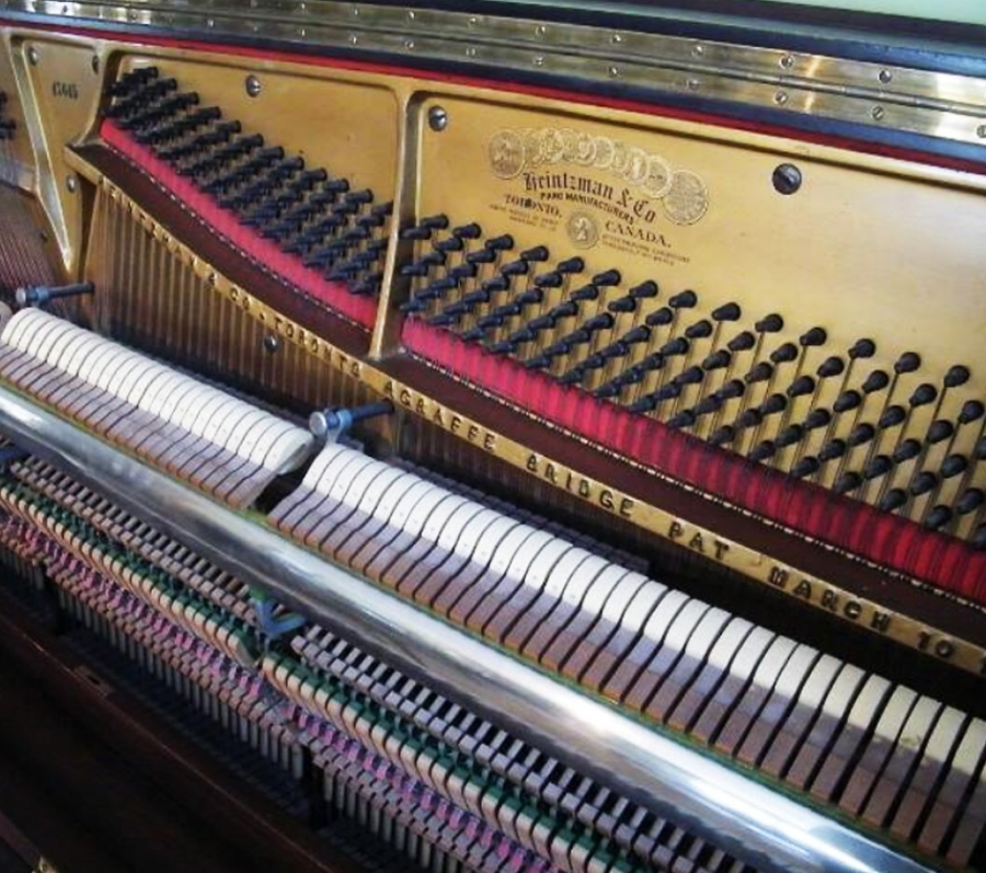 Interior view of an upright piano with its front panel removed, showing the tuning pins, strings, hammers, and action mechanism. The metal plate is engraved with the manufacturer’s name, and rows of felt‑covered hammers and wooden components are visible in detail.