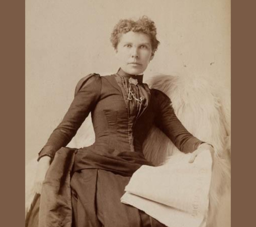 A vintage sepia-toned portrait of Alice Freeman-Brown seated in an elegant pose. She wears a long, fitted dress with puffed sleeves and decorative details along the bodice. One arm rests on a fur-draped chair, while the other holds a folded piece of fabric or a cloth across her lap. The background is plain, highlighting the formal style of the period clothing.