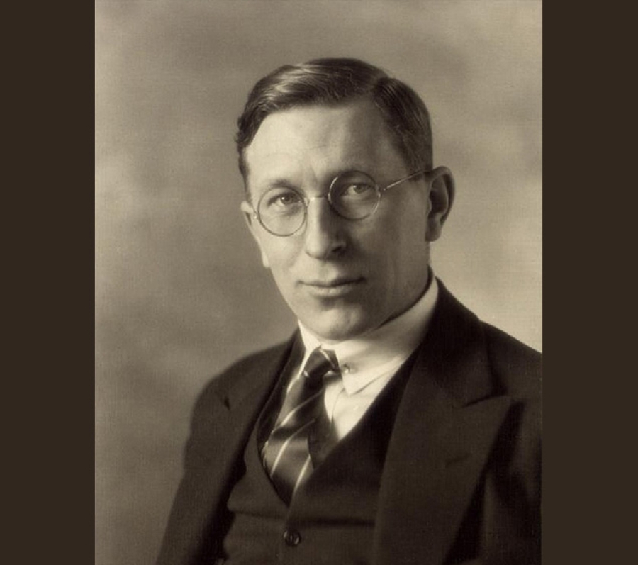 A vintage studio portrait of Frederick Banting wearing a dark three‑piece suit with a collared shirt and striped tie. The subject is posed against a softly lit, neutral background, creating a classic early‑20th‑century photographic style.