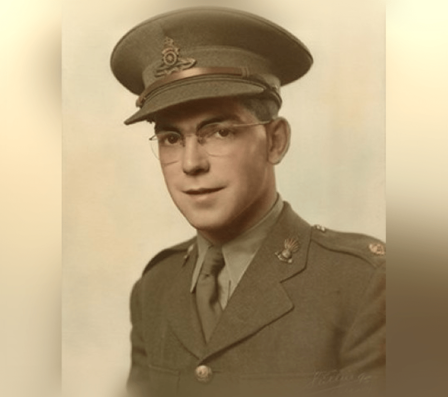 Colour portrait of a person wearing a military uniform and peaked cap, shown from the chest up against a light, softly graduated background. The uniform includes a tie, lapel insignia, and decorative pins, suggesting a formal service portrait.