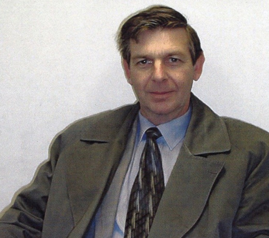 Person seated indoors wearing a coat and tie, holding a document.