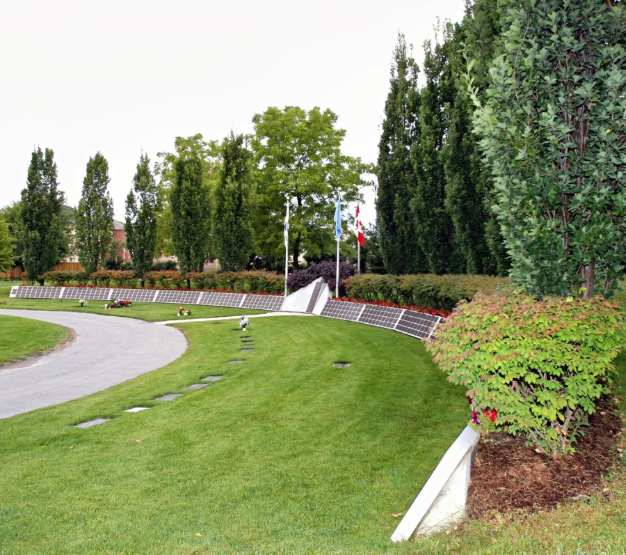 Curved path with memorial plaques and flags in a landscaped cemetery.