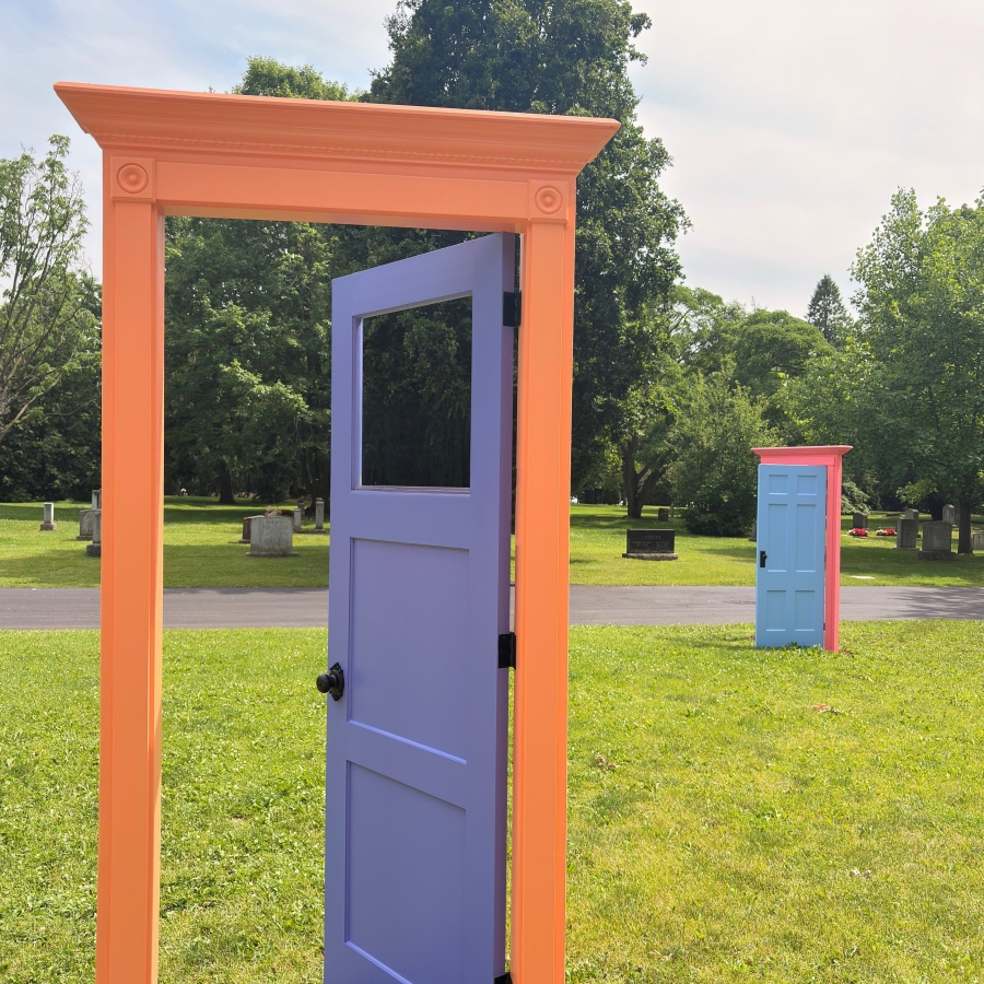Decorative purple door set within an orange doorframe on a grassy lawn, with trees and a pathway in the background.