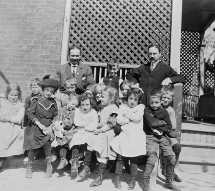 two men in suits standing with a group of young kids