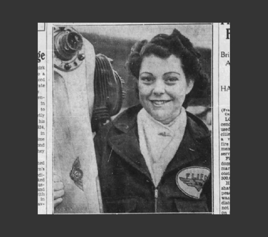 A black‑and‑white photograph showing Marion Alice Powell-Orr wearing a jacket with an aviation‑themed patch on the chest. They stand beside an aircraft propeller and engine assembly, holding one side of the propeller. The image has a vintage, historical appearance.