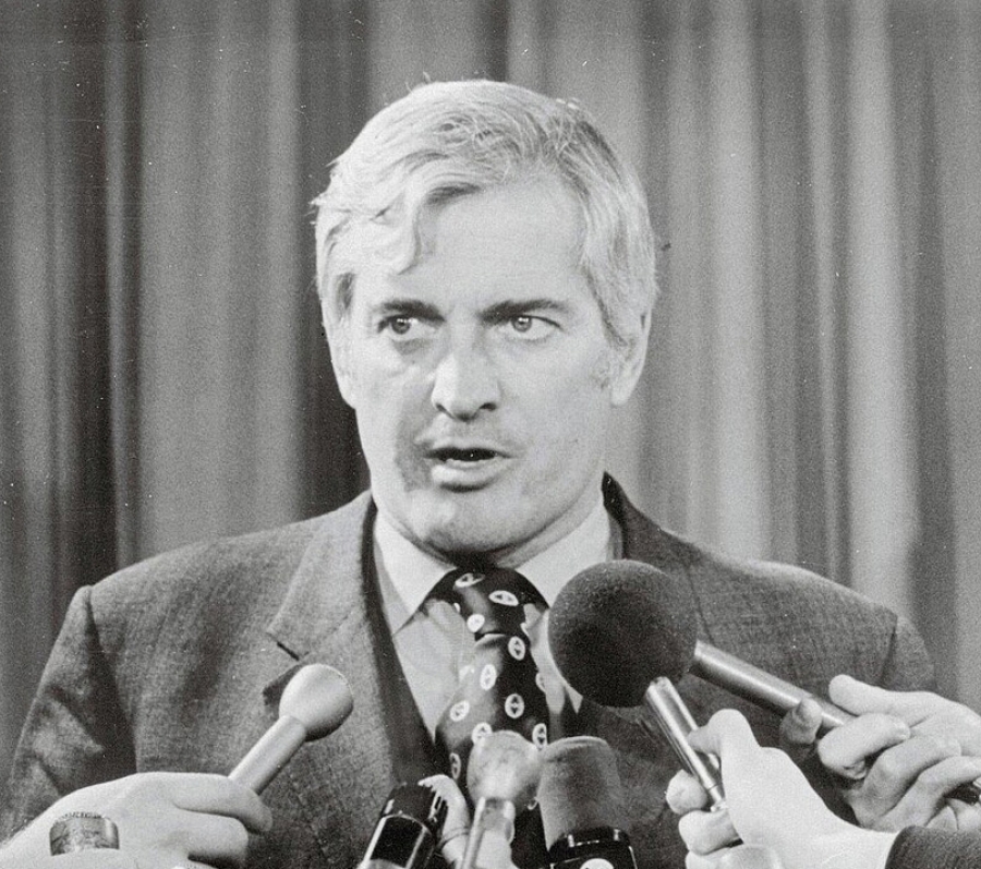 grey haired man with microphones in his face