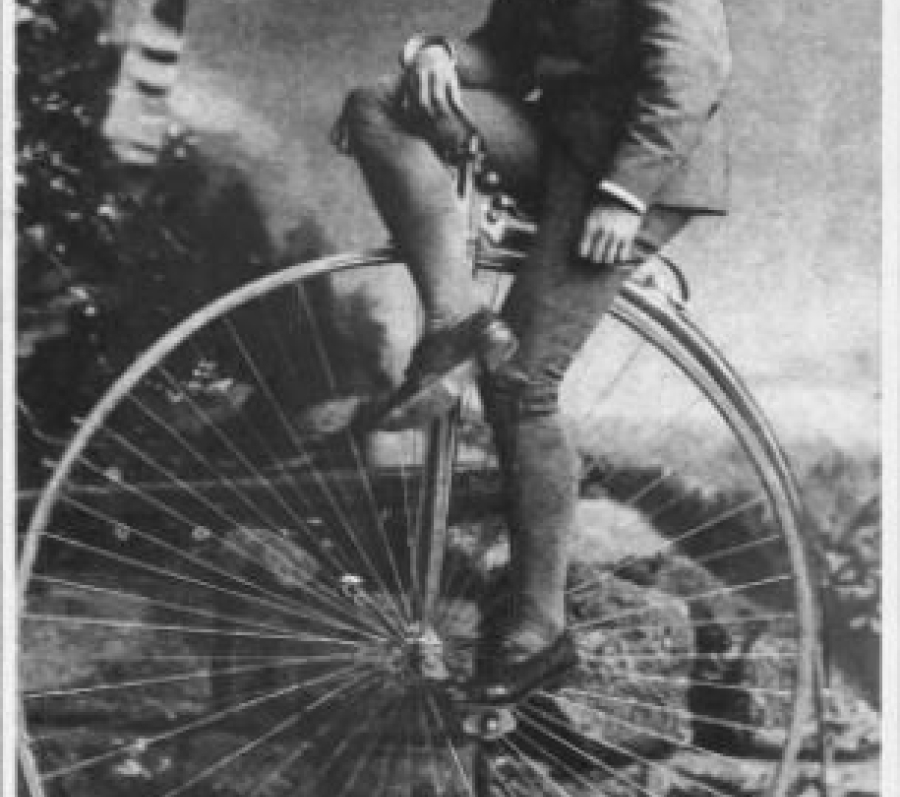 man sitting on an old bicycle with a huge wheel