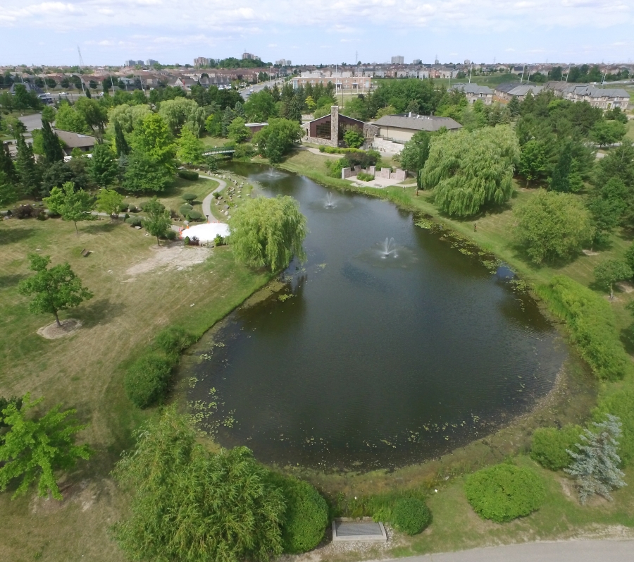 Image 1 (Aerial view): An aerial view of the Meadowvale Cemetery Garden of Remembrance featuring a large oval pond with a small fountain, and winding pathways. The image features an impressive arborteum of mature trees, surrounded by green lawns and buildings in the distance.