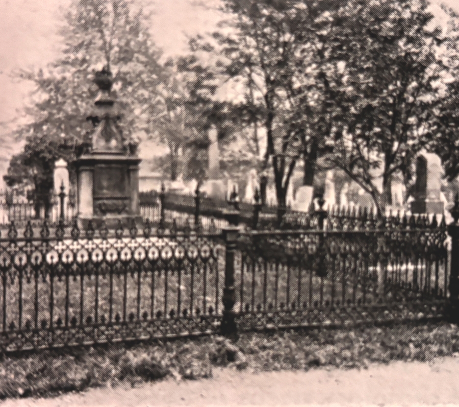 A historic cemetery plot enclosed by an ornate wrought-iron fence surrounds a raised stone monument belonging to George Brown, one of the founding fathers of Confederation. Mature trees and old gravestones are visible in the background.