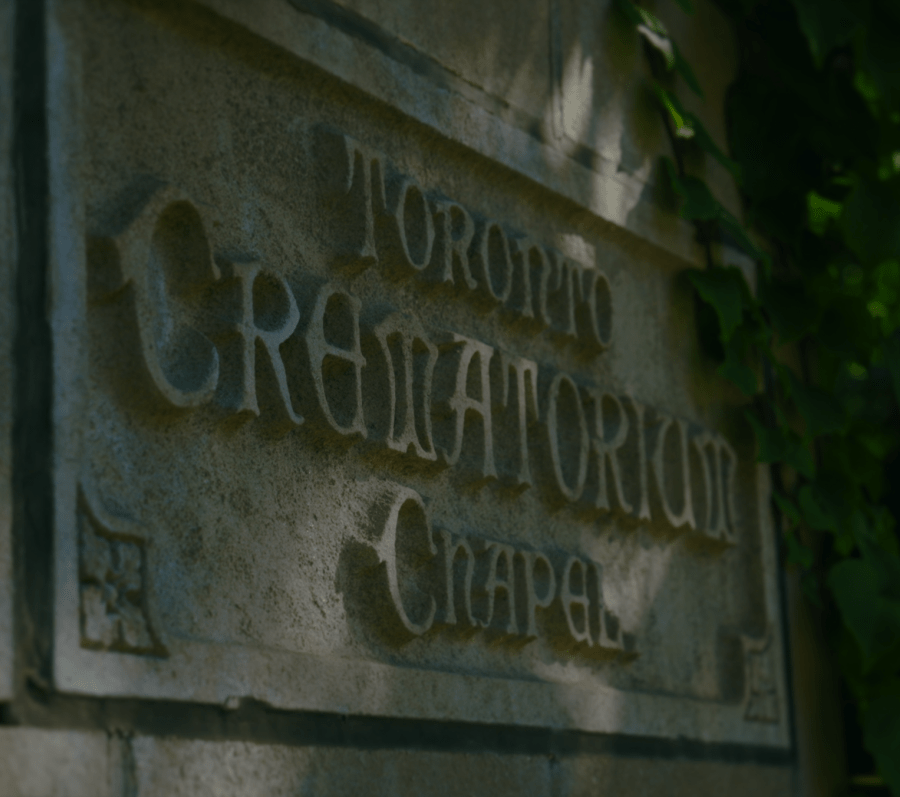Close‑up of carved stone signage reading “Toronto Crematorium Chapel,” partially framed by green ivy growing along the edge of the building.