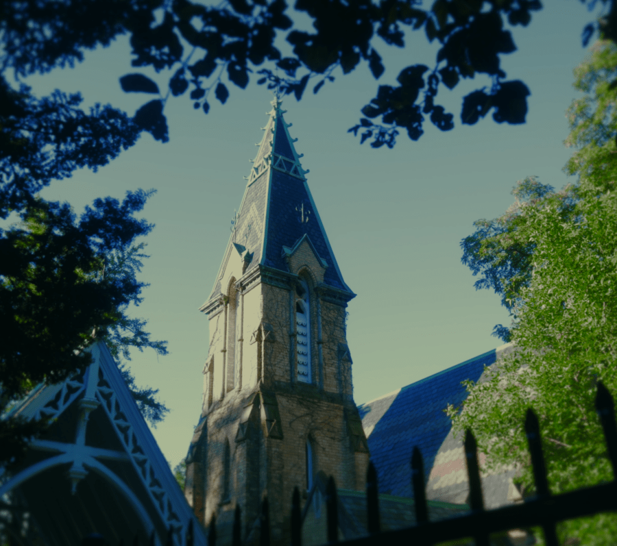 View of the Toronto Crematorium Chapel, a Gothic‑style stone building with a tall central tower, seen through tree branches and a wrought‑iron fence in a leafy, sunlit setting.
