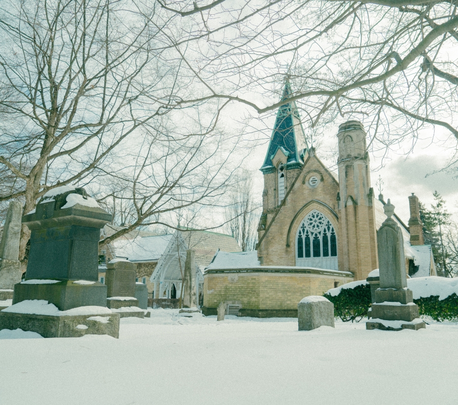 Winter view of the Toronto Crematorium and Necropolis Chapel, showing the Gothic chapel surrounded by snow‑covered ground, headstones, and leafless trees within a historic cemetery.