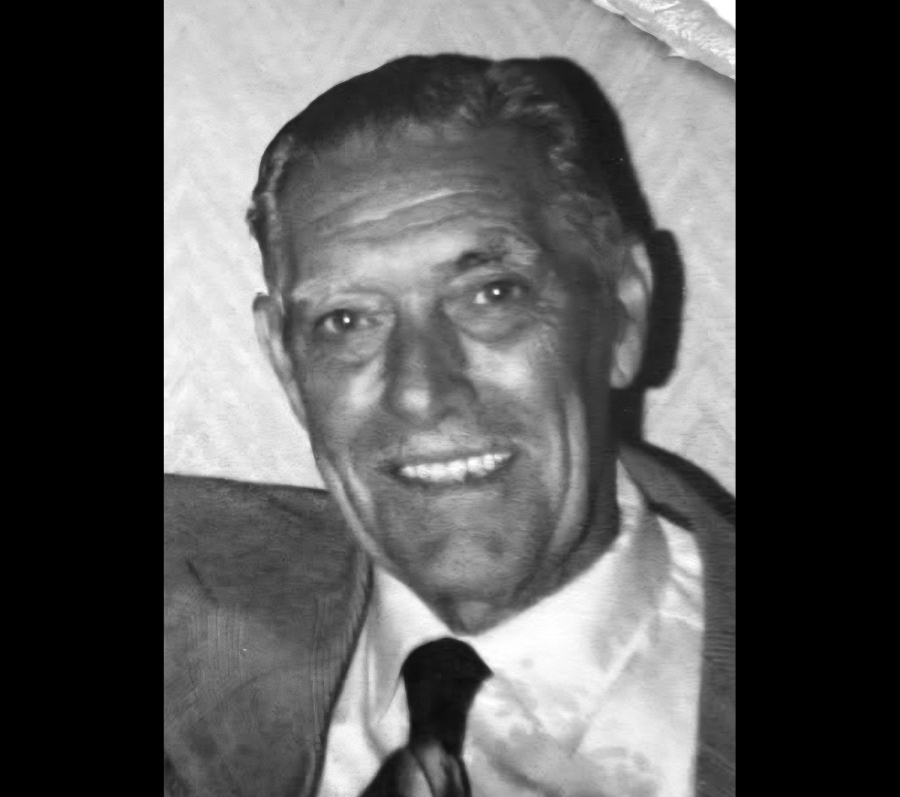 Black and white photo of Lloyd Shaddock. He is smiling and wearing a suit jacket, white shirt and black tie. His hair is well-kempt and short.