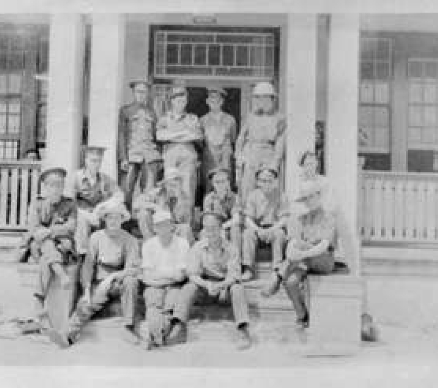 Black‑and‑white photograph of soldiers seated around tables inside a military convalescent hospital common room, with a nurse standing nearby and a piano against the wall, light streaming in through tall windows.