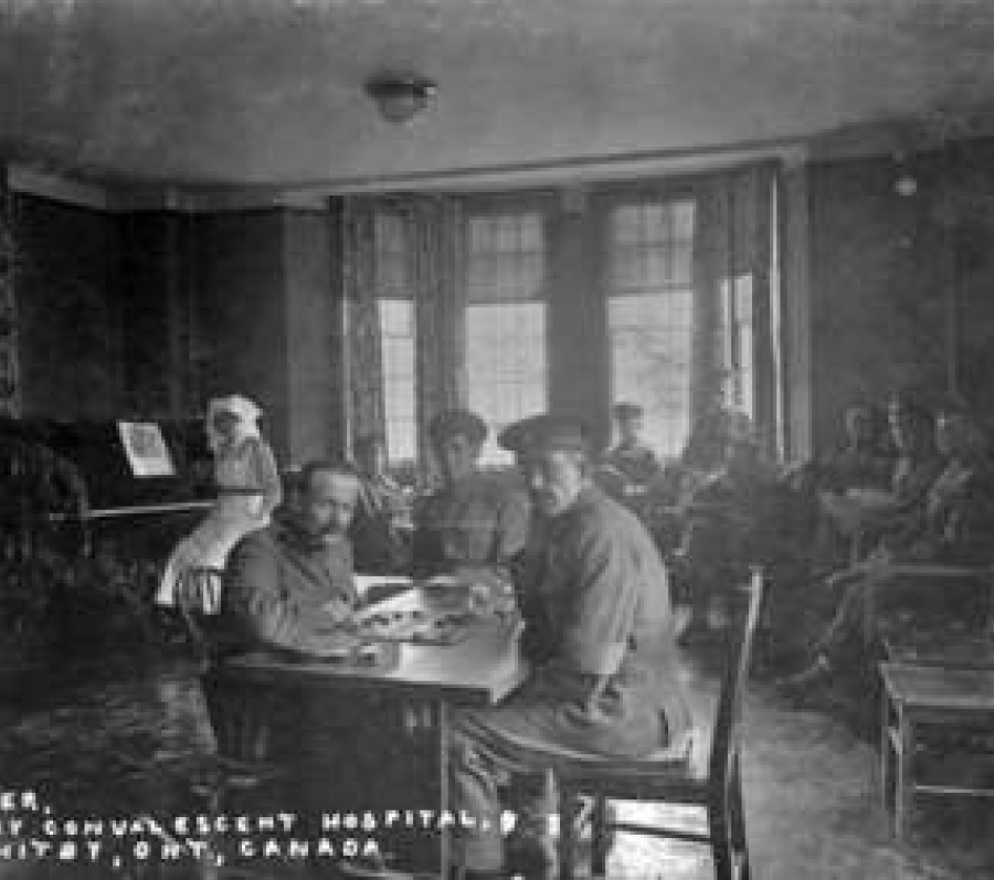 Black‑and‑white photograph of a group of uniformed soldiers gathered on the steps and porch of a large hospital building, some seated and others standing, posed informally in front of tall doors and columns.