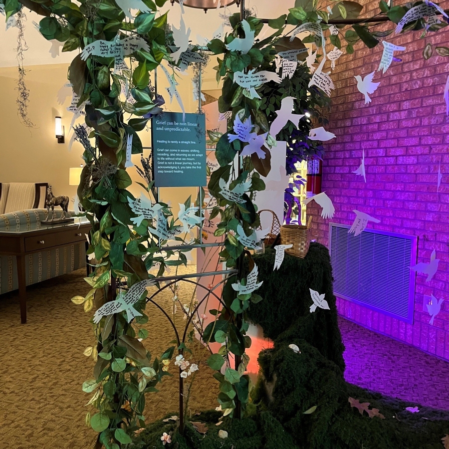 Memory Garden arch decorated with greenery and paper butterfly messages, illuminated by soft purple lighting.
