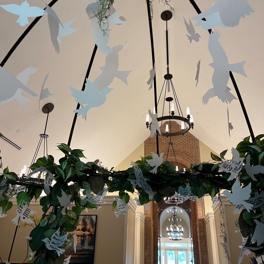 Paper butterfly messages hanging from a greenery-covered Memory Garden arch inside a chapel-like space.