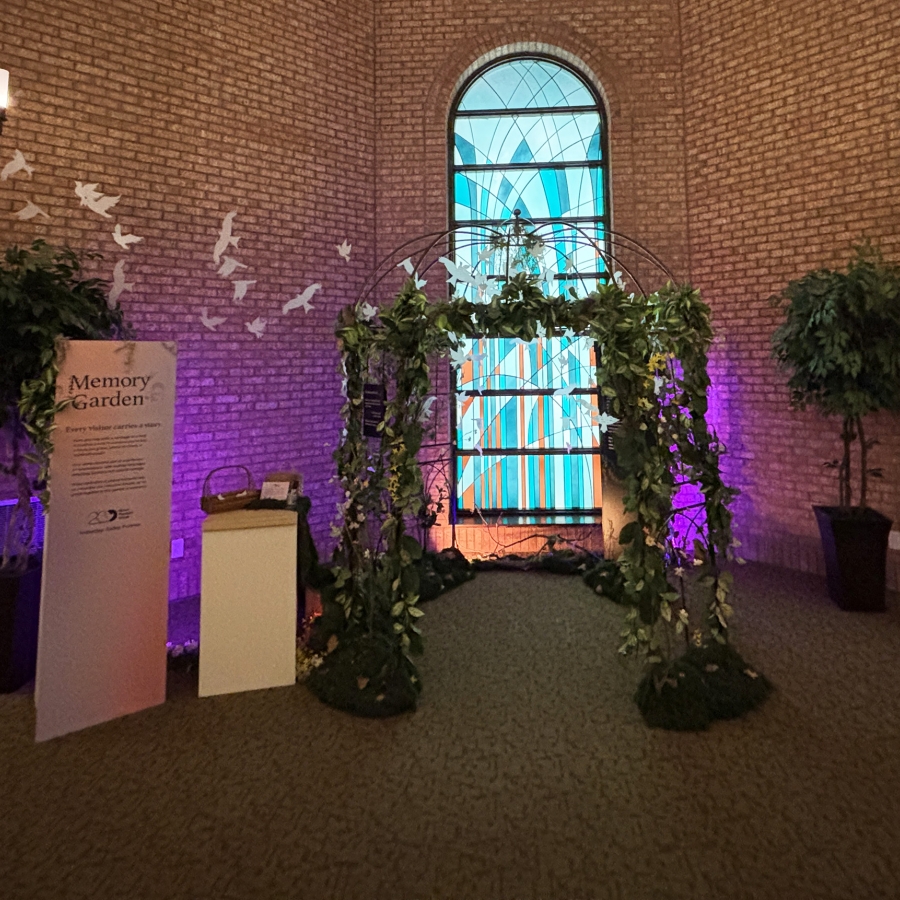 Memory garden display with leafy arch and stained-glass window backdrop.