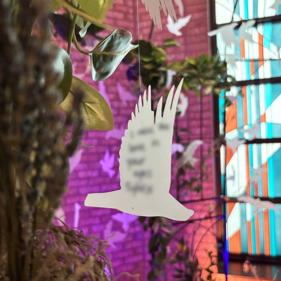 White bird-shaped ornament hanging among green leaves with colorful lighting in the background