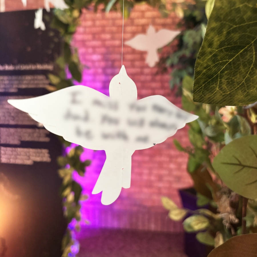 White bird-shaped ornament hanging in front of greenery with soft colored lighting