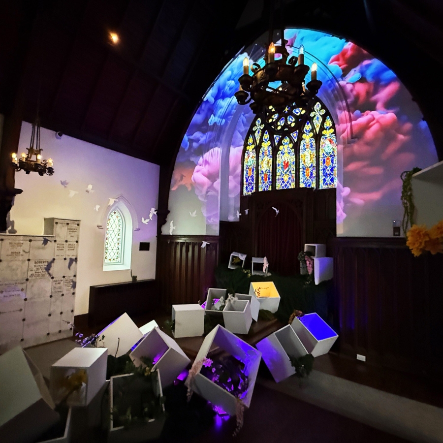 Chapel interior with stained glass, colorful light projection, and display boxes in foreground