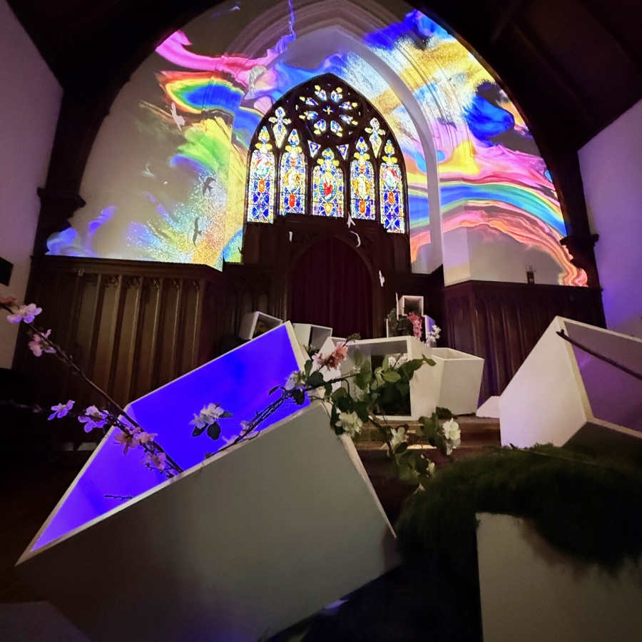 Chapel interior with stained glass and vivid rainbow light projection over altar and display