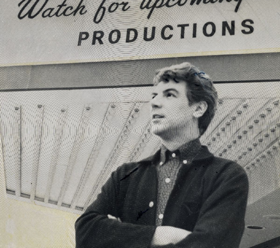 A duotone image in black and yellow showing a young man with his arms crossed, looking slightly upward with a sense of optimism. A sign on the wall behind him reads "Watch for upcoming productions".
