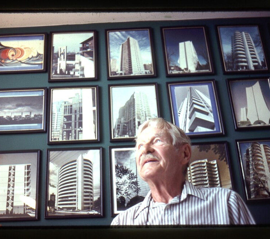 man standing behind a wall with framed photos of buildings