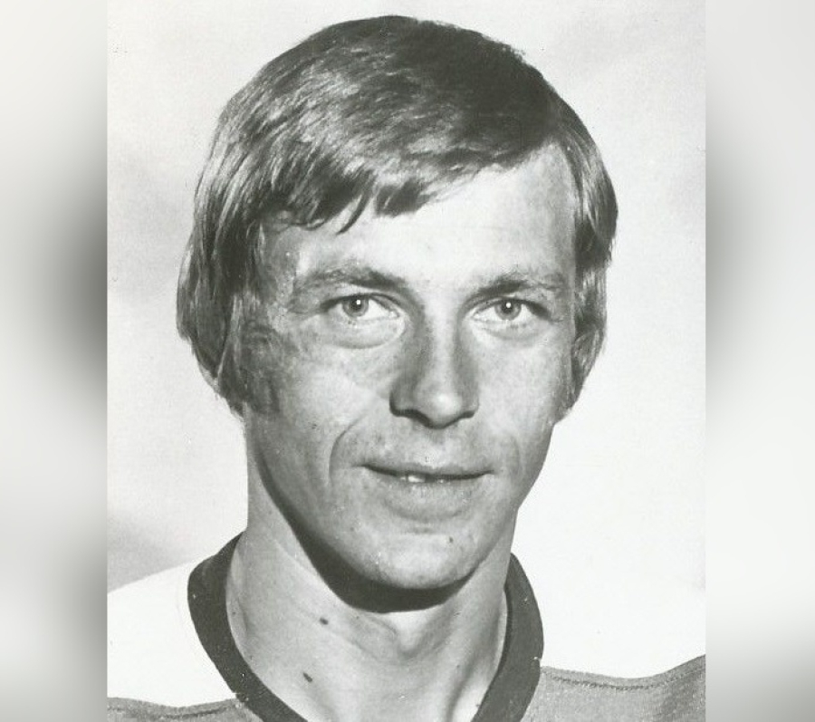 Black‑and‑white portrait of Nick Harbaruk shown from the shoulders up, with medium‑length hair parted to the side, wearing a collared athletic‑style shirt, photographed against a plain light background.