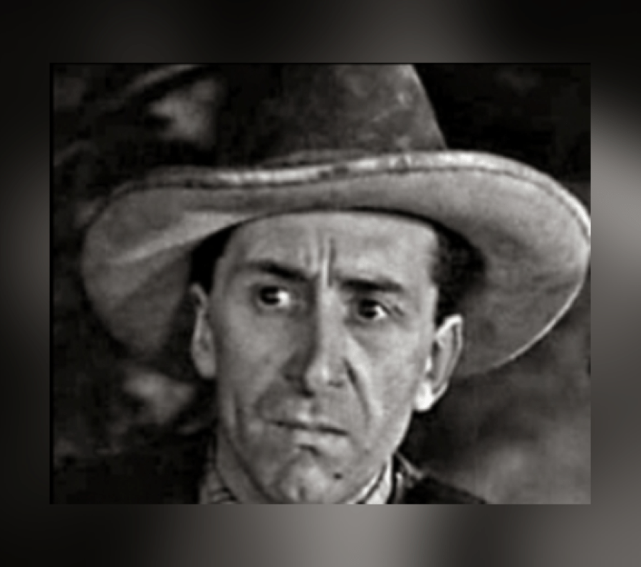 Black‑and‑white portrait of Eric Clavering wearing a wide‑brimmed hat and dark coat, shown from the shoulders up against a softly out‑of‑focus background.