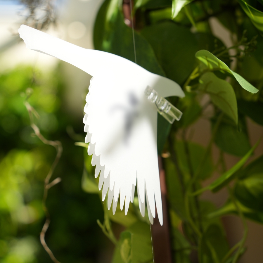 White bird-shaped hanging ornament among green leaves
