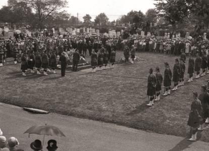 Large graveside service with uniformed mourners gathered in a cemetery.
