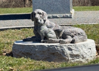 Stone sculpture of a resting dog on a memorial base.
