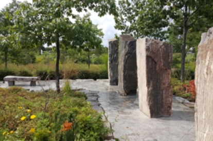 Tall upright stone slabs arranged along a paved garden path with trees and greenery.