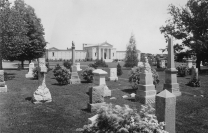 Historic cemetery with stone monuments and mausoleum in the background.