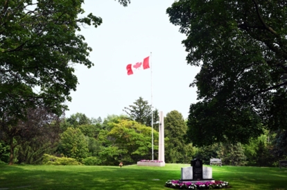 Canadian flag flying above a memorial monument in a landscaped park.