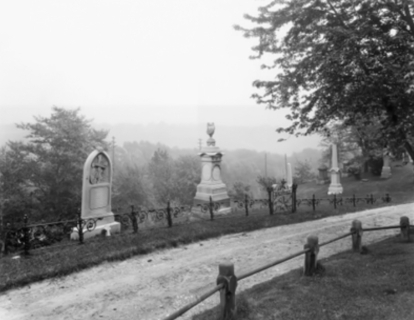 Gravel road through a cemetery with stone monuments on a hillside.