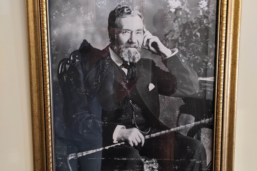 Black-and-white portrait of an older man seated, holding a cane, in a gold frame.