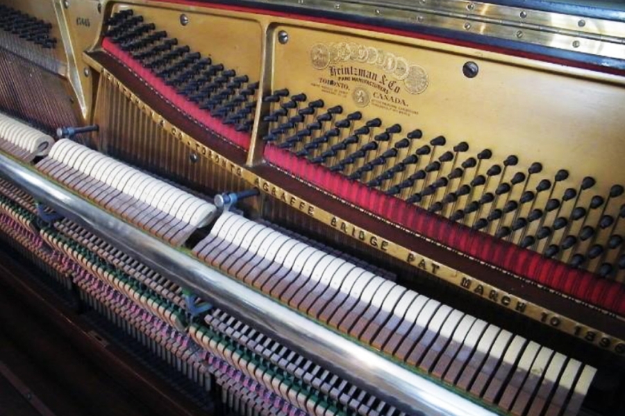 Interior view of an upright piano with its front panel removed, showing the tuning pins, strings, hammers, and action mechanism. The metal plate is engraved with the manufacturer’s name, and rows of felt‑covered hammers and wooden components are visible in detail.