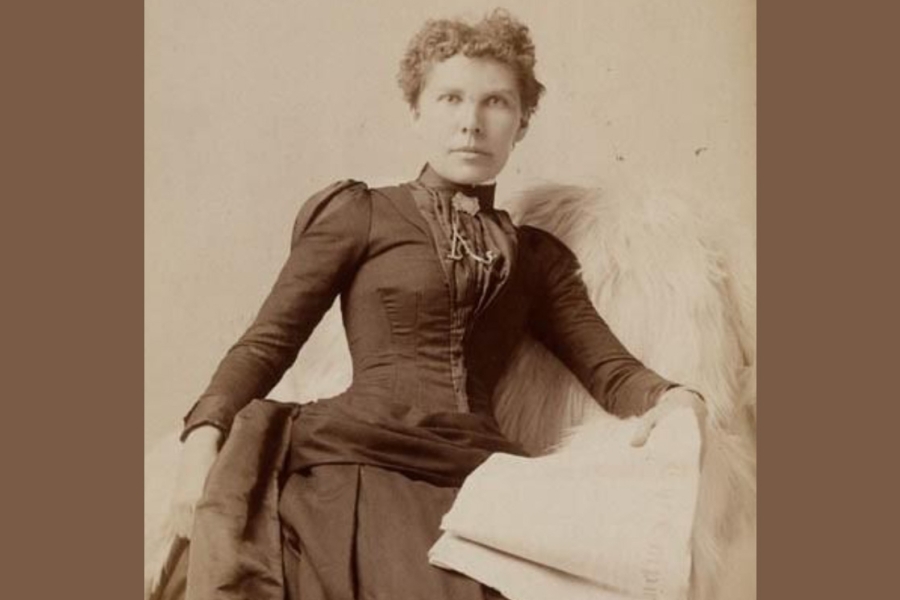 A vintage sepia-toned portrait of Alice Freeman-Brown seated in an elegant pose. She wears a long, fitted dress with puffed sleeves and decorative details along the bodice. One arm rests on a fur-draped chair, while the other holds a folded piece of fabric or a cloth across her lap. The background is plain, highlighting the formal style of the period clothing.