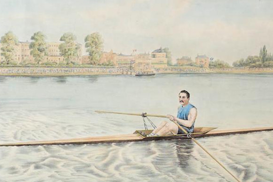 A lone rower in a blue sleeveless shirt navigates a narrow wooden sculling boat across calm water, leaving gentle ripples behind. A row of large trees and historic-looking buildings line the far riverbank beneath a bright, lightly clouded sky.