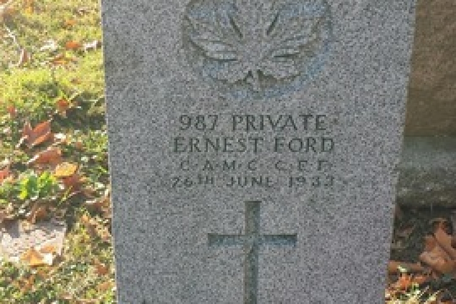 Gravestone of Private Ernest Ford with engraved cross and emblem, set in a grassy cemetery with fallen leaves.