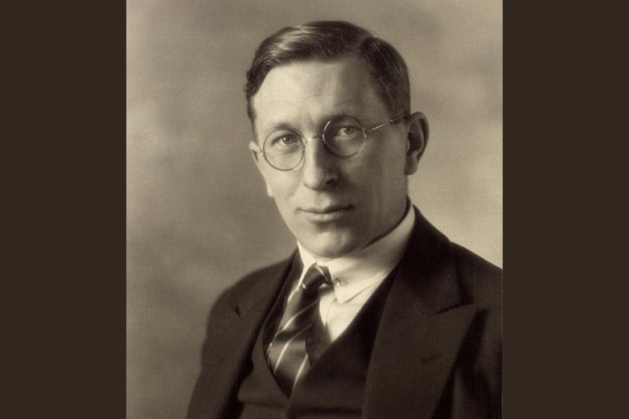 A vintage studio portrait of Frederick Banting wearing a dark three‑piece suit with a collared shirt and striped tie. The subject is posed against a softly lit, neutral background, creating a classic early‑20th‑century photographic style.