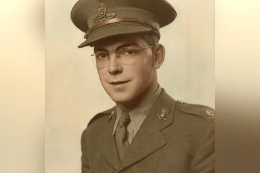 Colour portrait of a person wearing a military uniform and peaked cap, shown from the chest up against a light, softly graduated background. The uniform includes a tie, lapel insignia, and decorative pins, suggesting a formal service portrait.