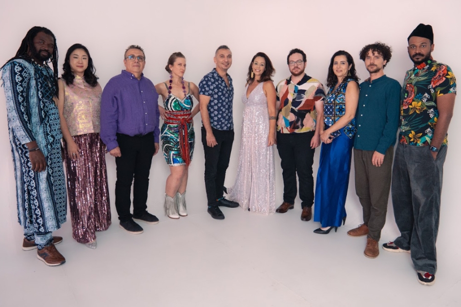 Group of people standing in a line against a plain background, dressed in colorful outfits.