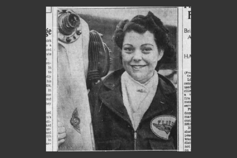 A black‑and‑white photograph showing Marion Alice Powell-Orr wearing a jacket with an aviation‑themed patch on the chest. They stand beside an aircraft propeller and engine assembly, holding one side of the propeller. The image has a vintage, historical appearance.