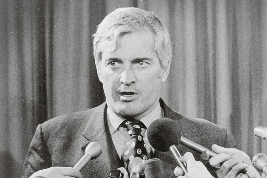 grey haired man with microphones in his face