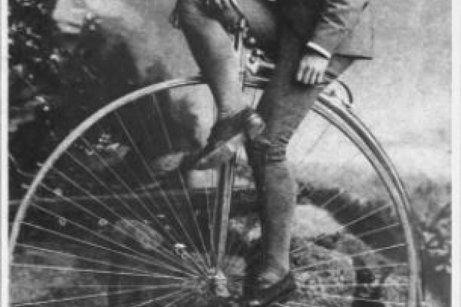 man sitting on an old bicycle with a huge wheel