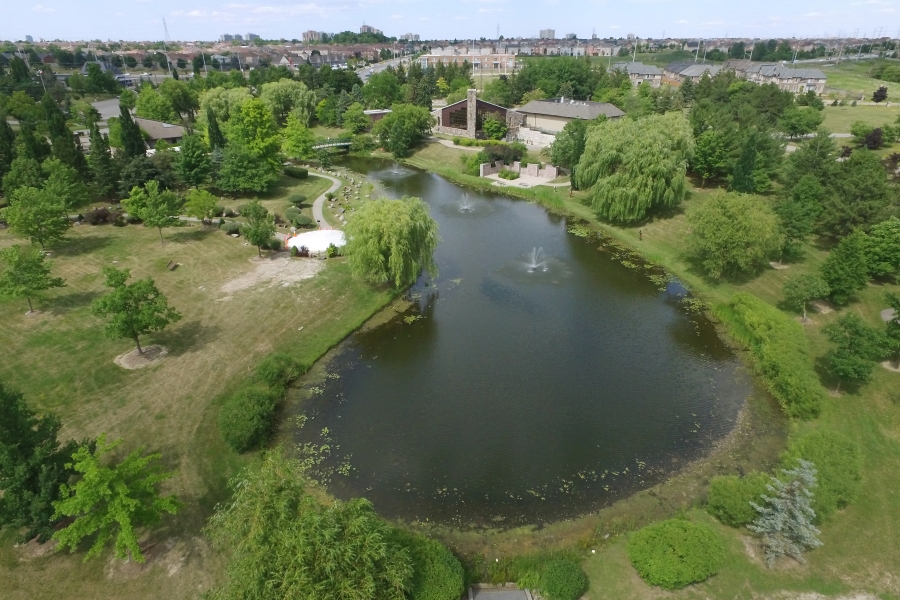 Image 1 (Aerial view): An aerial view of the Meadowvale Cemetery Garden of Remembrance featuring a large oval pond with a small fountain, and winding pathways. The image features an impressive arborteum of mature trees, surrounded by green lawns and buildings in the distance.