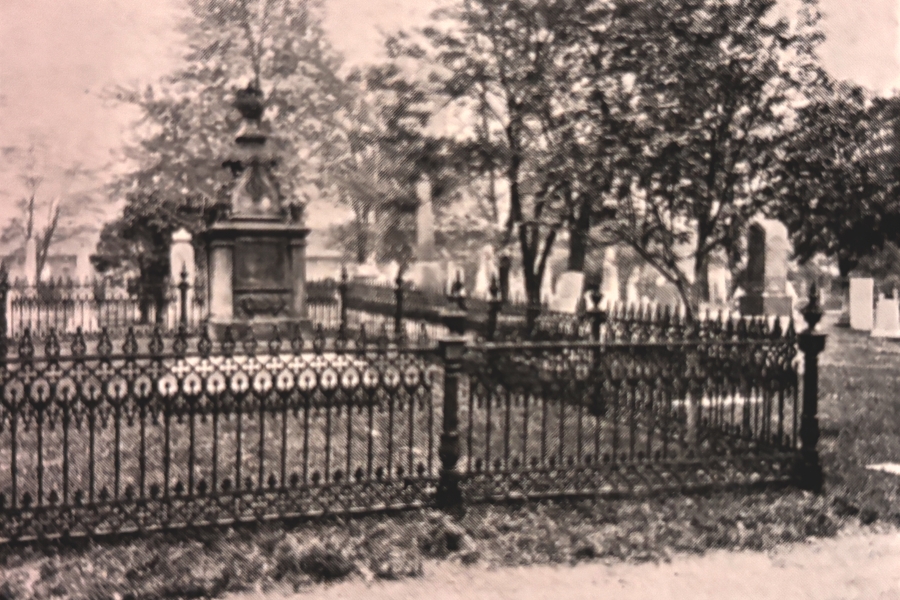 A historic cemetery plot enclosed by an ornate wrought-iron fence surrounds a raised stone monument belonging to George Brown, one of the founding fathers of Confederation. Mature trees and old gravestones are visible in the background.